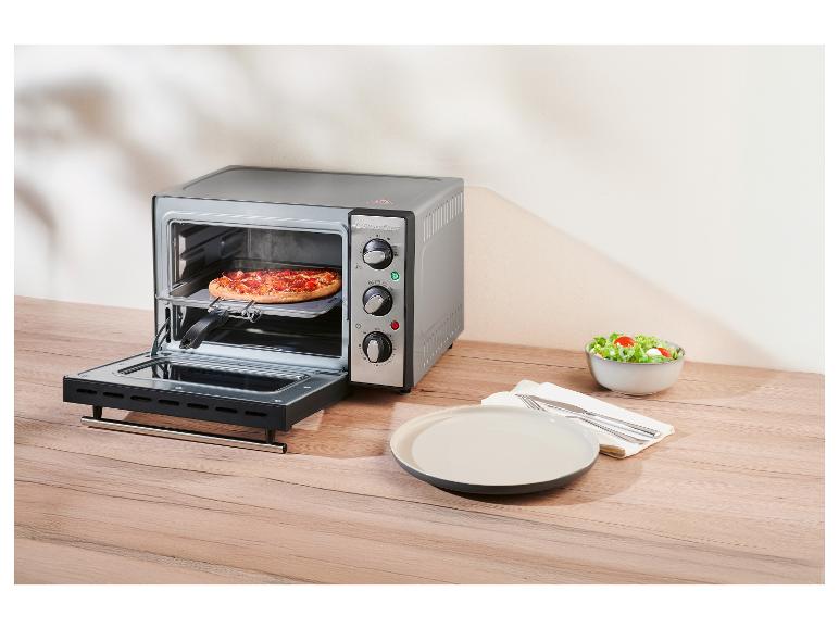 Mini piekarnik SilverCrest z pizzą w środku, obok talerza i miski sałatkowej.