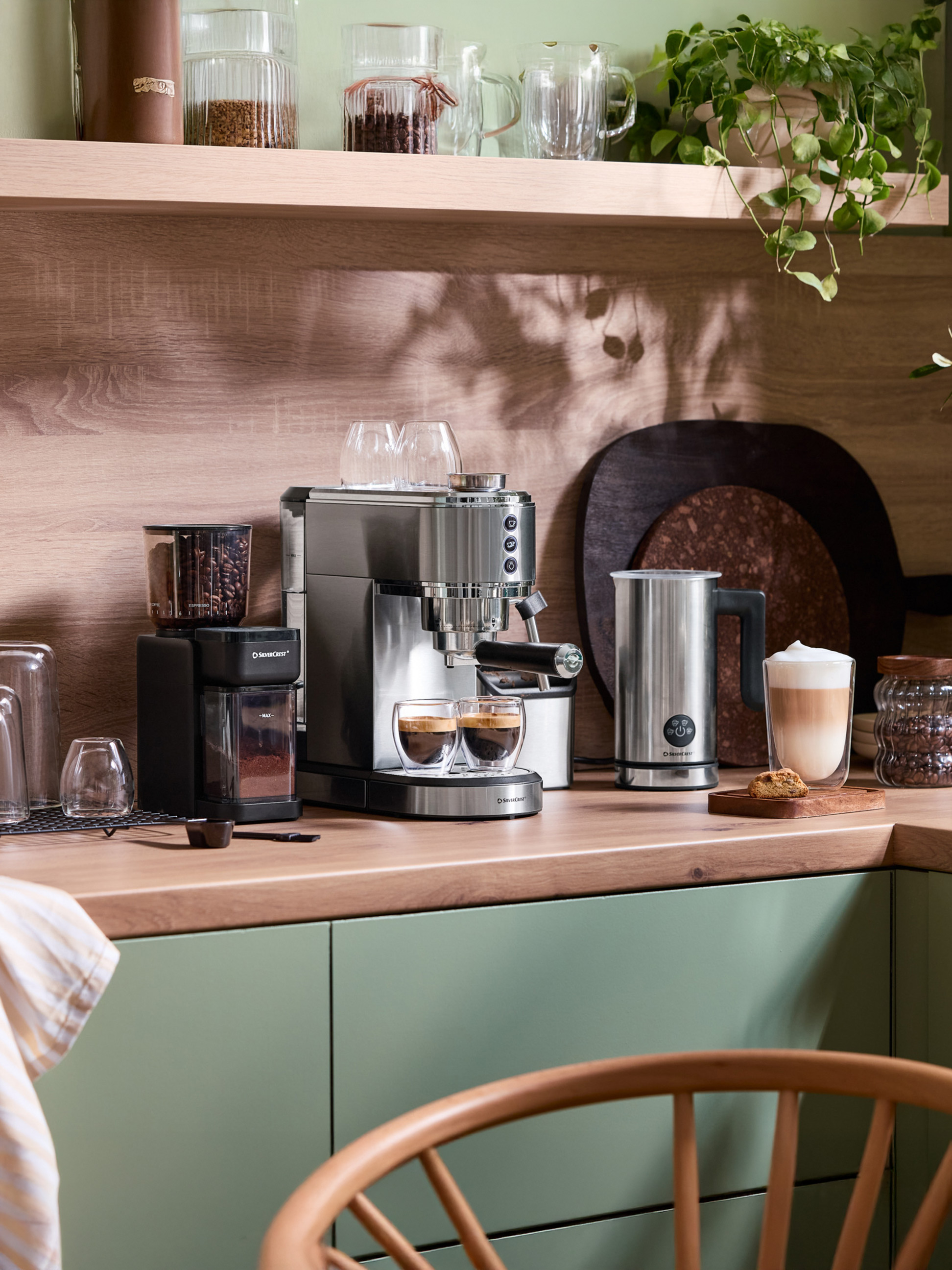 Ekspres do kawy SilverCrest i młynek na drewnianym blacie kuchennym z zielonymi szafkami.