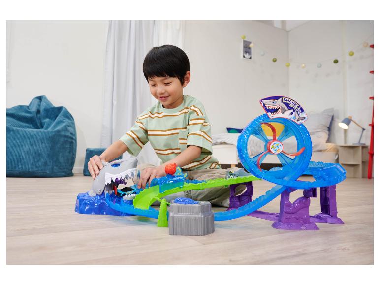 Chłopiec bawi się zestawem Hot Wheels Shark Cyclone na podłodze.