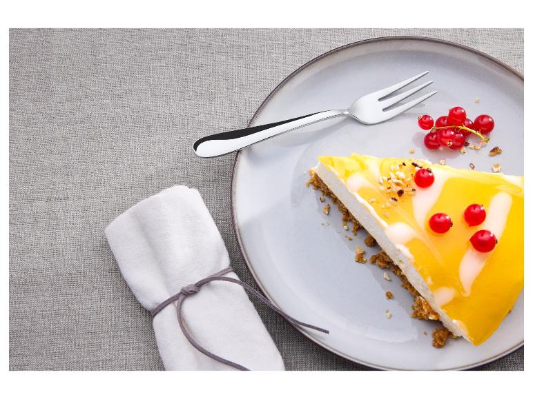 Kawałek sernika z polewą mango i czerwonymi porzeczkami na talerzu z widelcem.