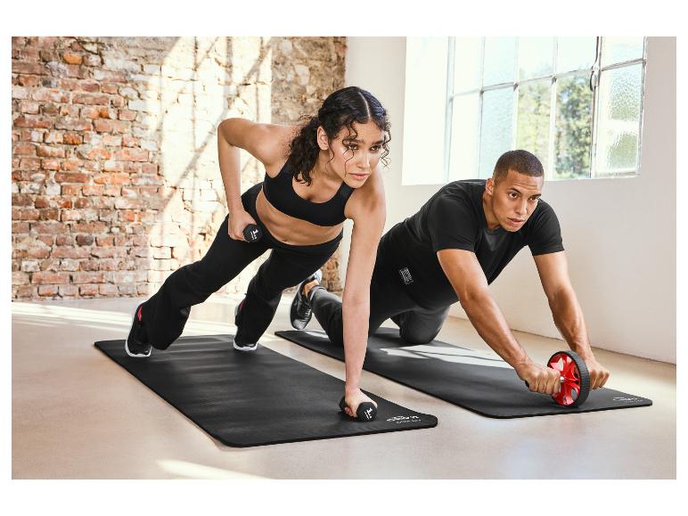 Dwie osoby ćwiczą z kółkiem do brzucha i hantle na macie do ćwiczeń.