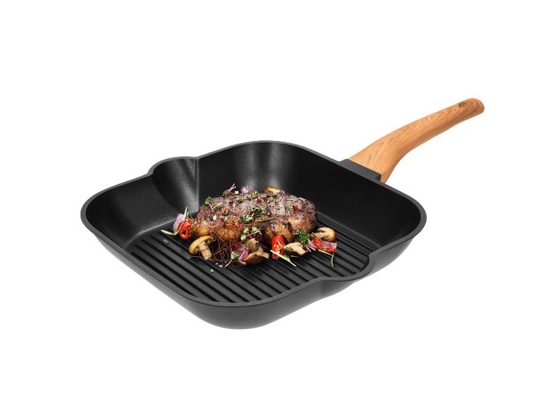 Grillowany stek z warzywami na czarnej kwadratowej patelni grillowej z drewnianą rączką.