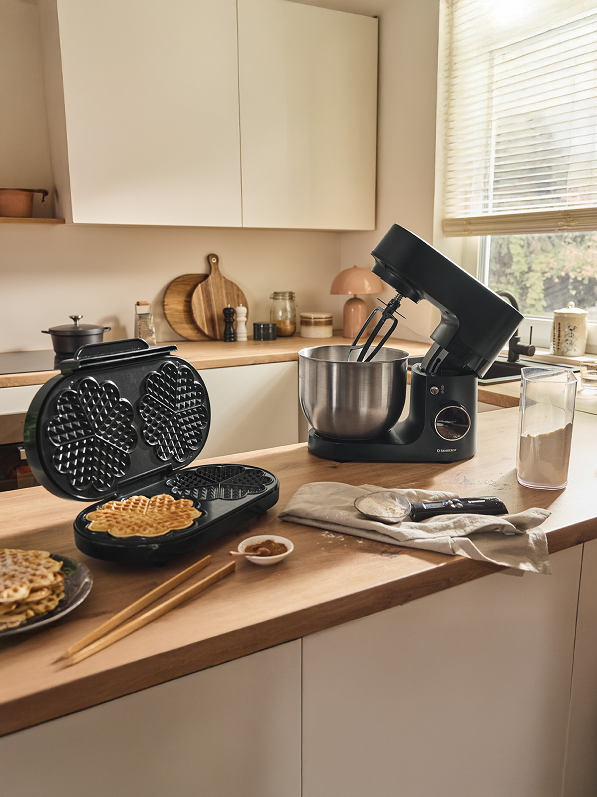 Gofrownica i czarny mikser kuchenny na drewnianym blacie, z gotowymi goframi.