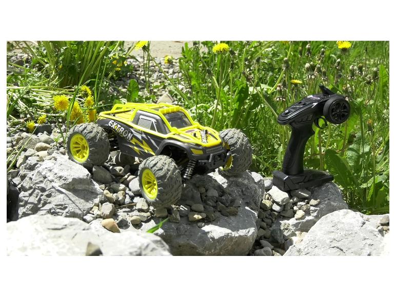 Żółto-czarny samochód Extron zdalnie sterowany na kamieniach, z pilotem obok.