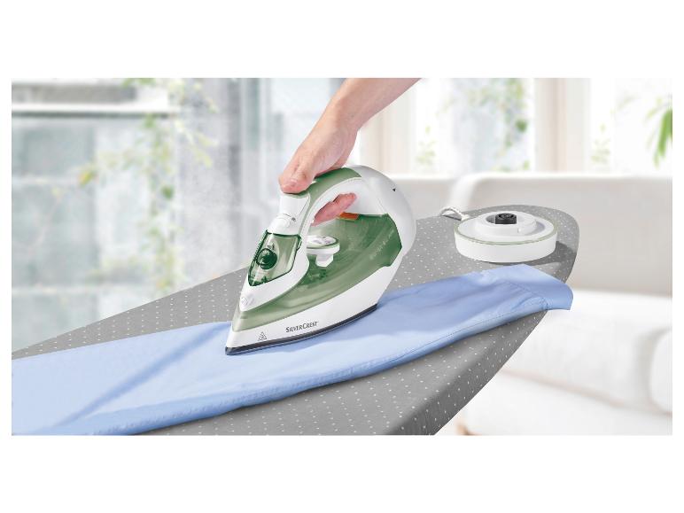 Zielone żelazko parowe Silvercrest na desce do prasowania, prasowanie niebieskiej bluzki.