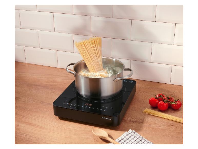 Gotowanie spaghetti w garnku na płycie indukcyjnej, pomidory i surowe spaghetti na blacie.