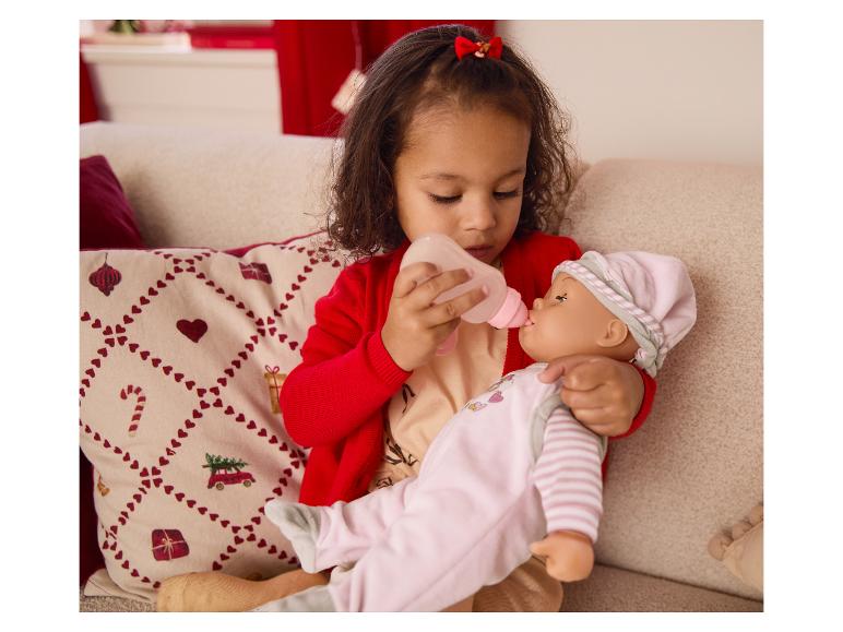 Młoda dziewczynka karmi lalkę butelką na sofie.