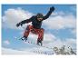 Snowboardzista w czarnej kurtce i czerwonych wzorzystych spodniach w powietrzu z górami