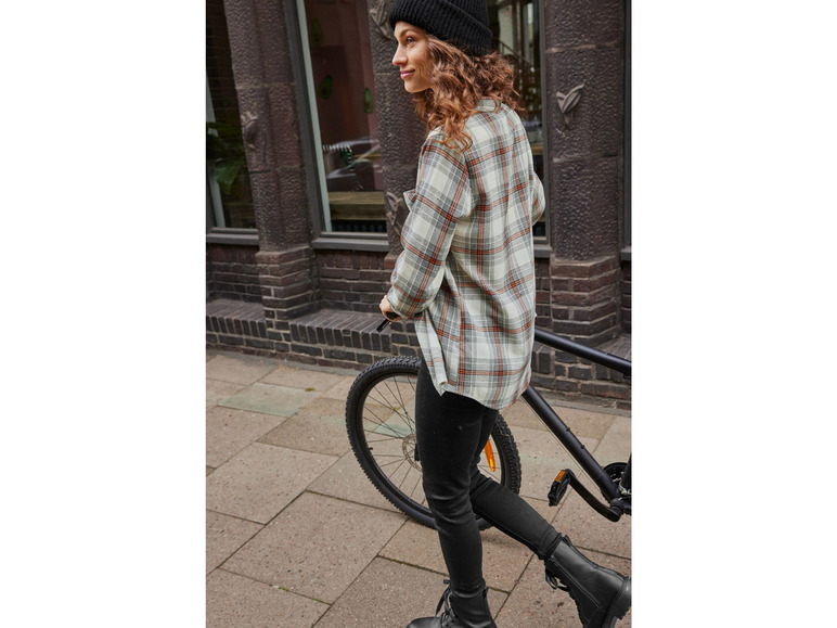 Kobieta w kratkowanej koszuli jedzie na rowerze.