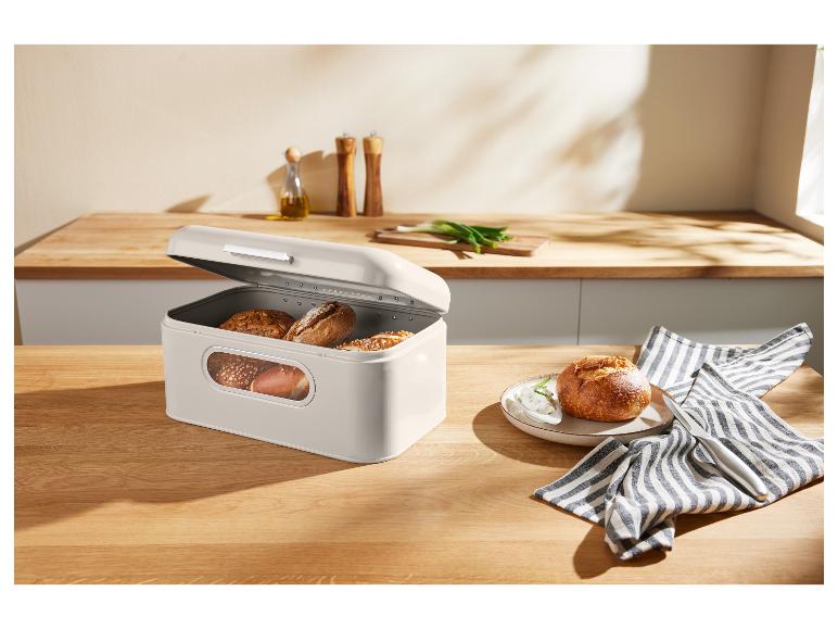 Beżowy chlebak z pieczywem na drewnianym stole w kuchni.