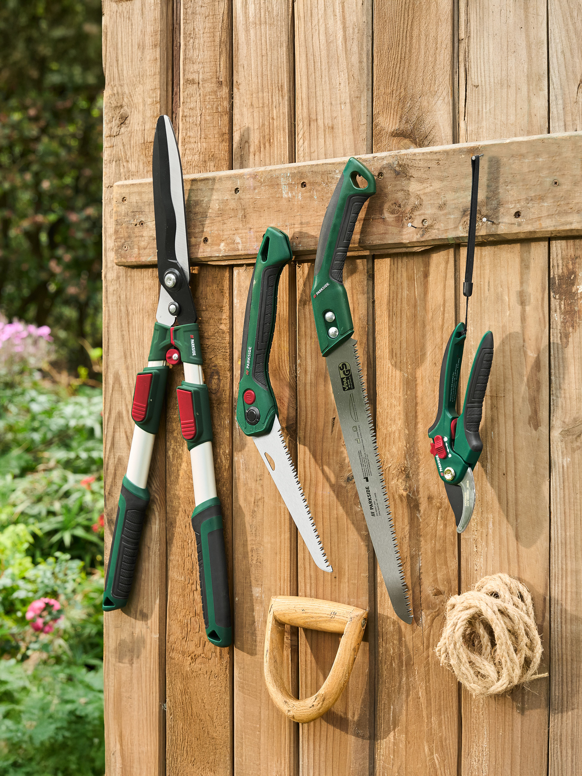 Nożyce ogrodowe, piły i sekatory PARKSIDE wiszące na drewnianym płocie.