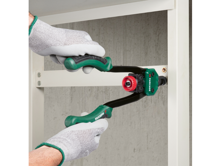 Osoba w rękawiczkach używająca nitownicy do mocowania nita do metalowej półki.