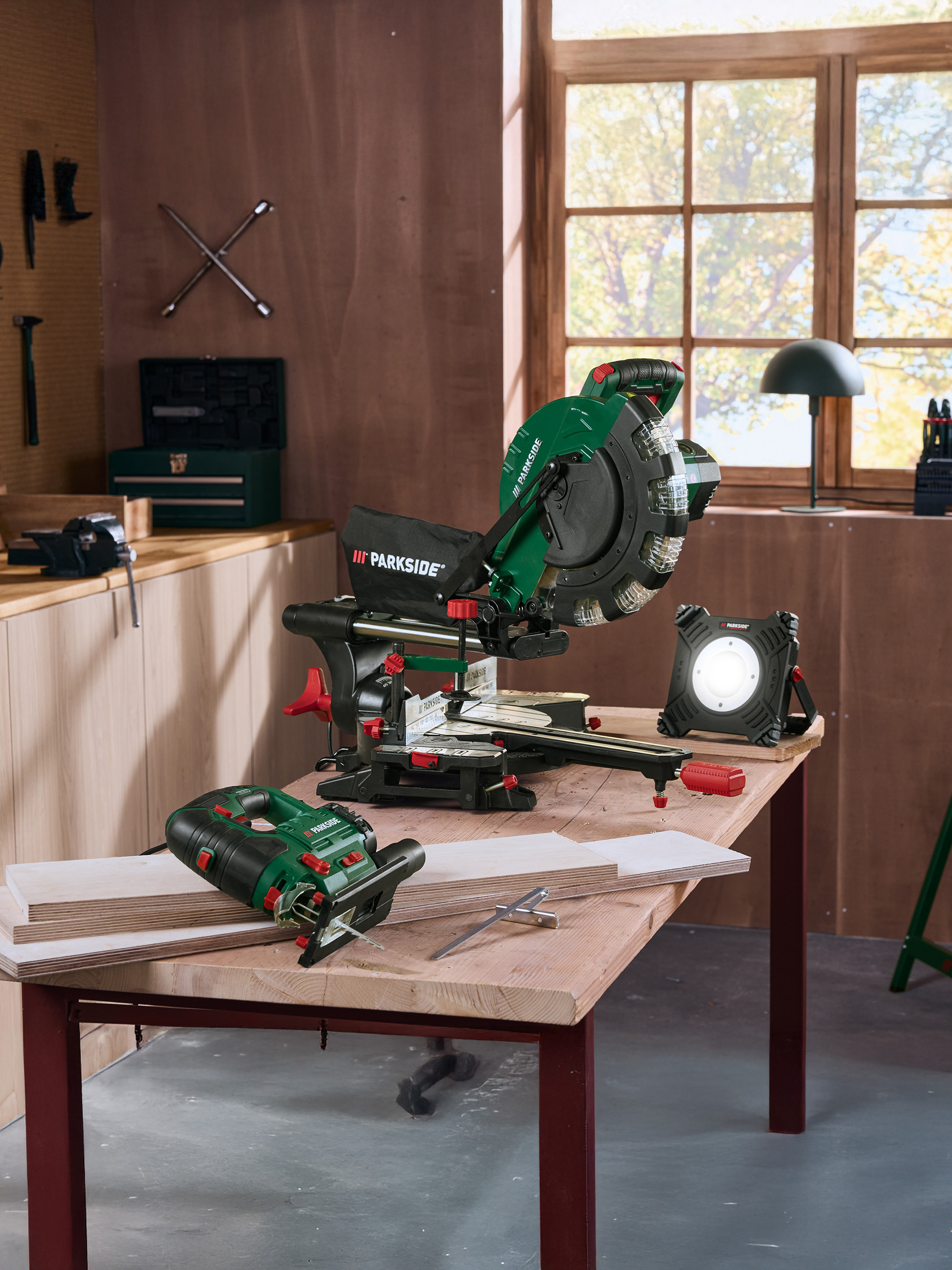 Narzędzia Parkside: ukośnica, wyrzynarka i lampa robocza na drewnianym stole w warsztacie.