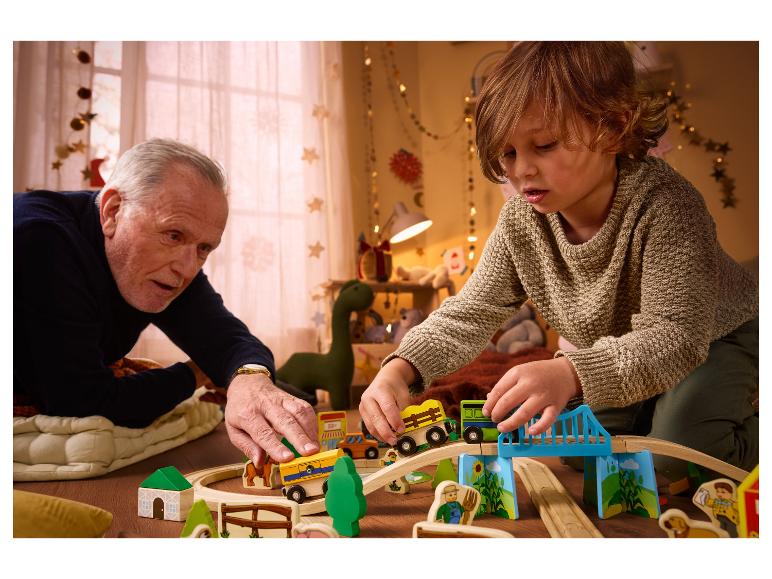 Dziecko i dorosły bawią się drewnianymi pociągami i torami.