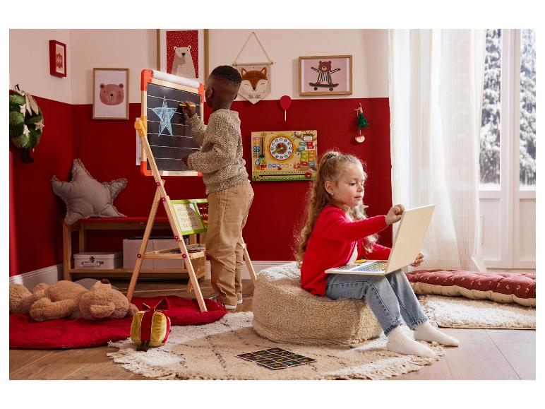 Dwoje dzieci bawi się w świątecznie udekorowanym pokoju: chłopiec rysuje na tablicy, dziewczynka korzysta z laptopa.