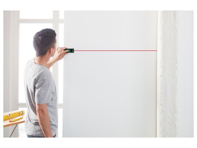 Mężczyzna używa dalmierza laserowego do mierzenia ściany.