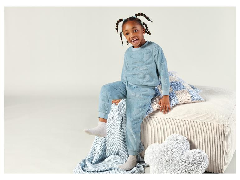 Dziewczynka w niebieskiej piżamie w gwiazdki siedzi na sofie z poduszkami.