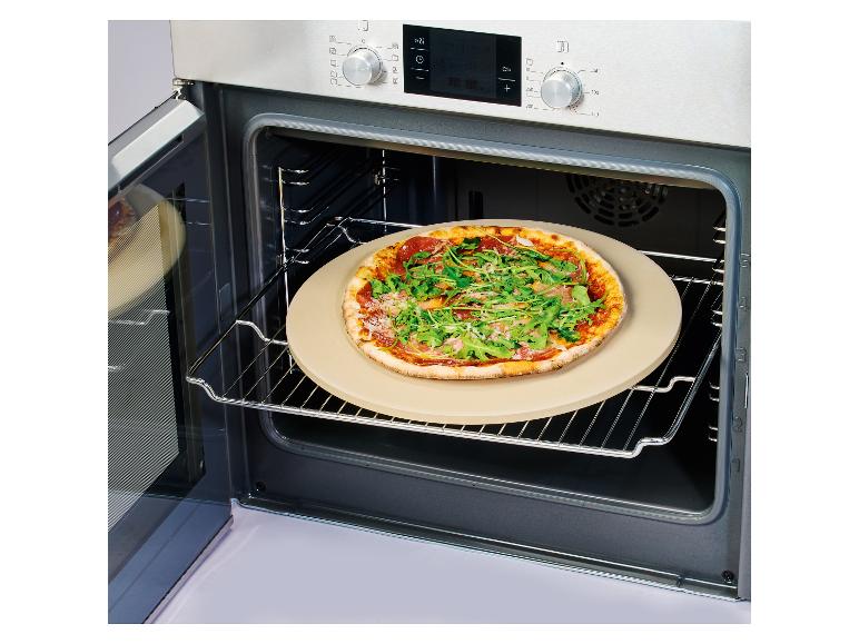 Pizza z rukolą i szynką na kamieniu do pizzy w otwartym piekarniku.