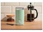 Miętowy młynek do kawy, kawiarka French Press i słoik z kawą mieloną na drewnianym stole.