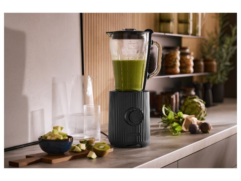 Czarny blender z zielonym koktajlem, owocami i ziołami w kuchni.