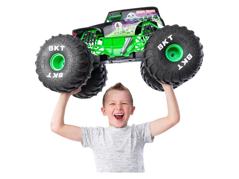 Chłopiec trzyma zabawkę monster truck Grave Digger Monster Jam nad głową.