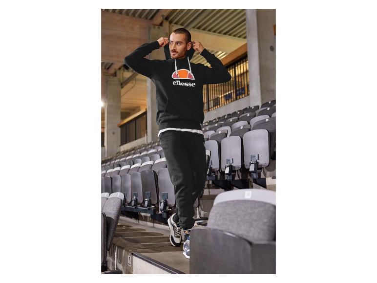 Mężczyzna w czarnej bluzie Ellesse i spodniach na stadionie.