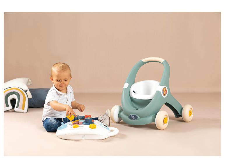 Dziecko bawi się tablicą aktywności i chodzikiem Little Smoby w tle.