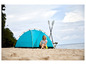 Kobieta siedzi przed niebieskim namiotem na plaży z dwoma wiosłami obok.
