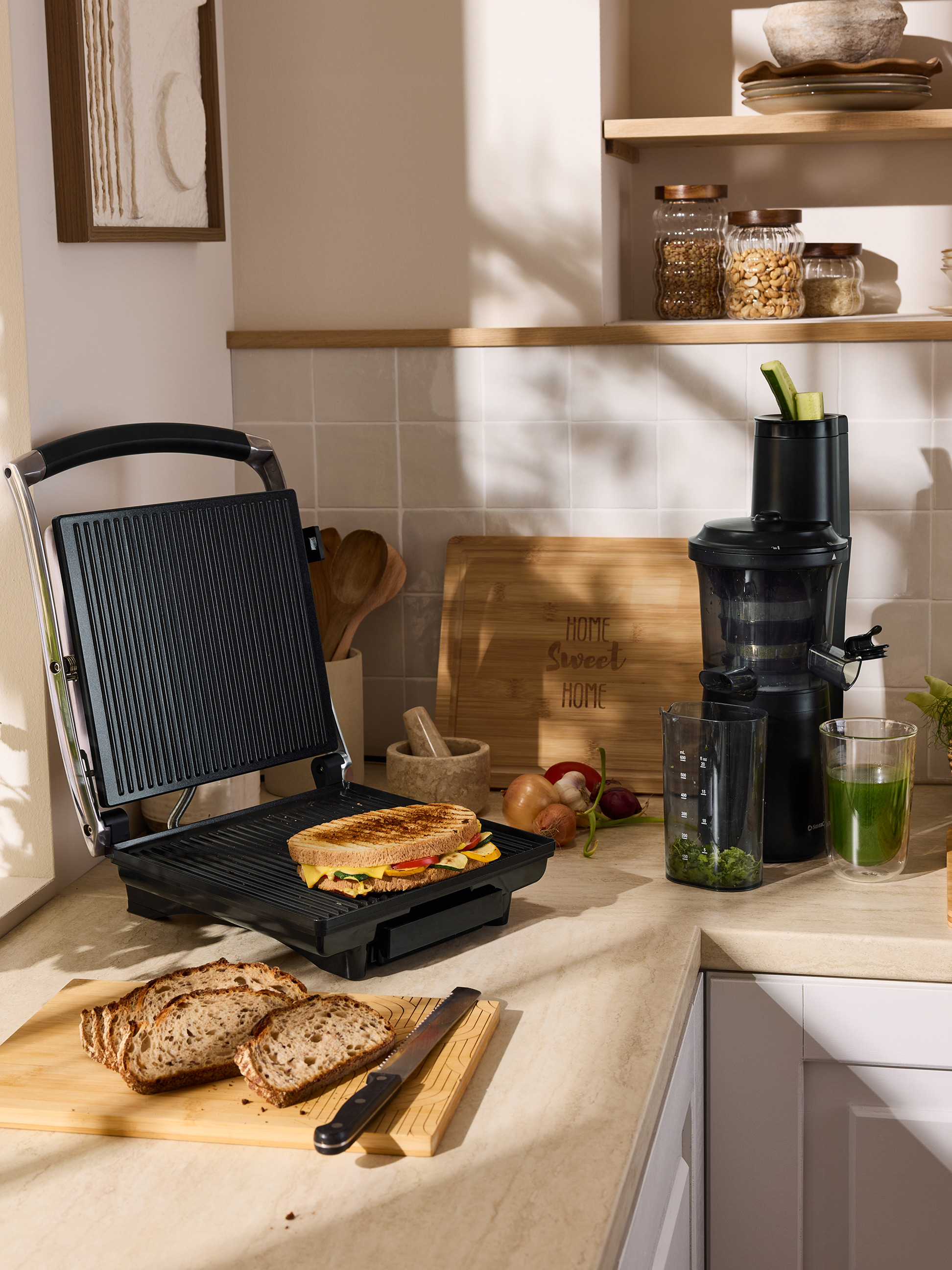 Grillowana kanapka na opiekaczu, pokrojony chleb i wyciskarka do soków na blacie kuchennym.