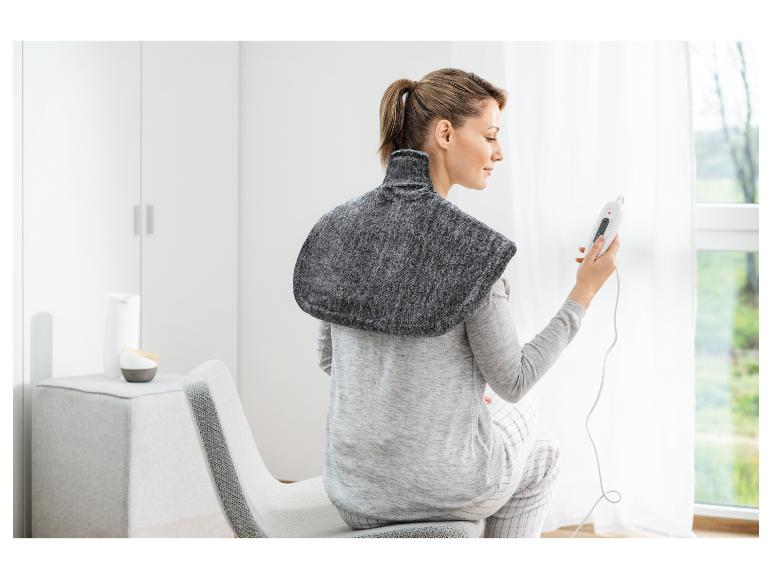 Kobieta w elektrycznej poduszce grzewczej na ramionach, trzymająca pilota.