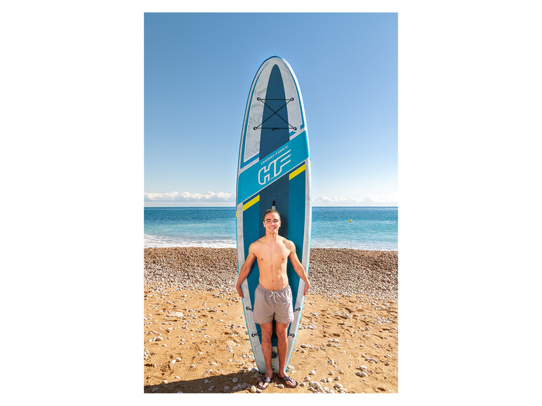 Mężczyzna pozuje z dmuchanym paddleboardem Hydro-Force na piaszczystej plaży.