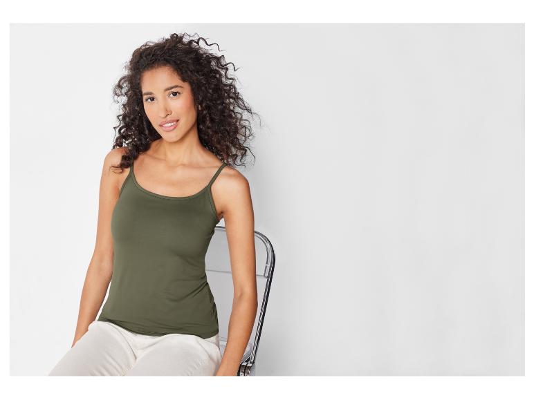Modelka w zielonej, cienkiej koszulce na ramiączkach i białych spodniach.