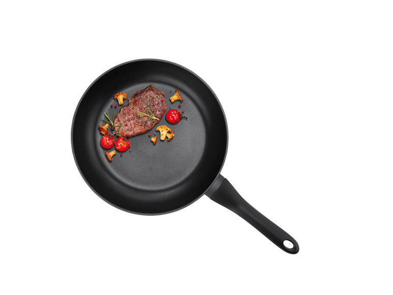 Czarna patelnia z grillowanym stekiem, grzybami i pomidorami cherry.