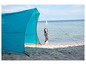 Niebieski namiot Outwell na plaży, obok którego idzie kobieta.