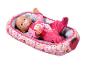 Lalka Baby Born w różowej piżamie ze smoczkiem, leżąca w miękkim, wzorzystym koszu.