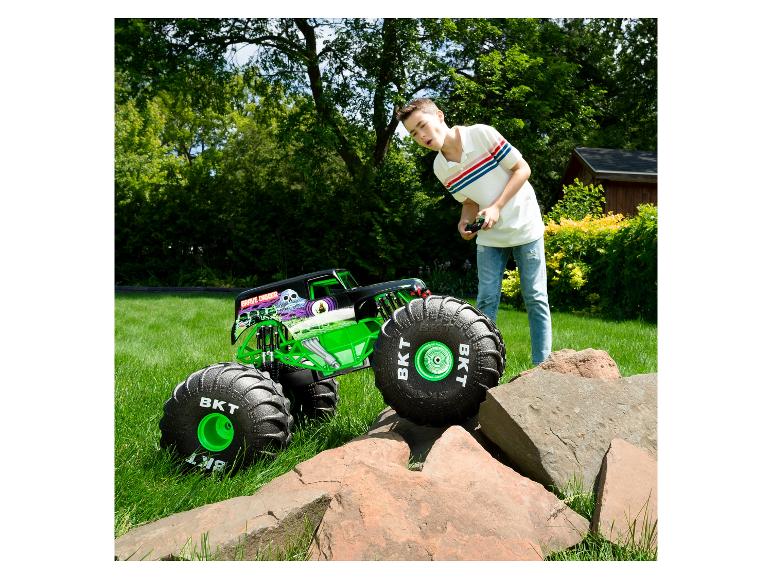 Chłopiec steruje zdalnie sterowanym monster truckiem Grave Digger na trawie, z kamieniami na pierwszym planie.