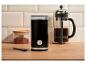 Czarny elektryczny młynek do kawy, French Press i słoik z kawą mieloną na drewnianym blacie.