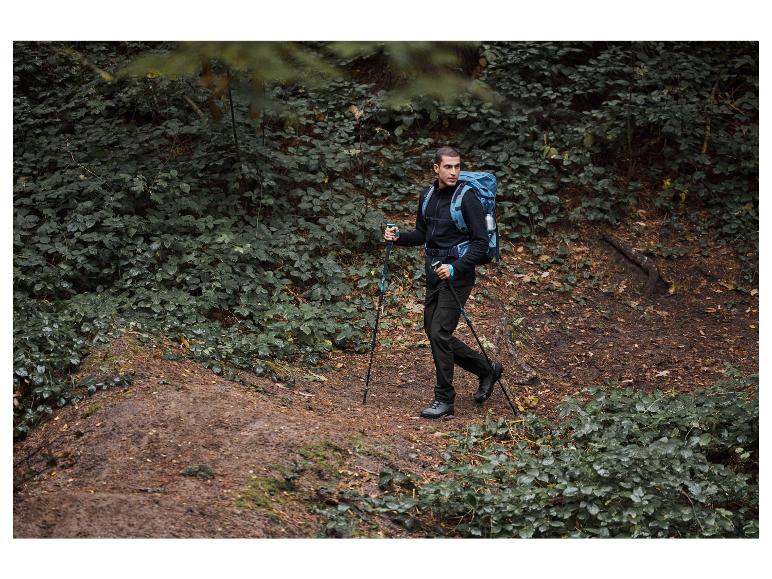 Mężczyzna idzie z plecakiem i kijkami po szlaku w lesie.