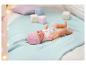 Lalka Baby Born z różową czapką i smoczkiem leży na niebieskim kocu.