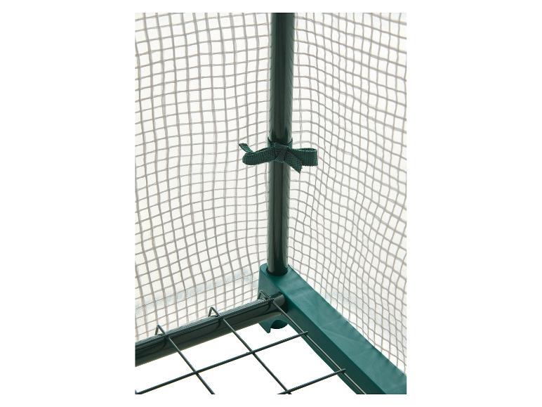 Szczegół szklarni ogrodowej z zieloną ramą i przezroczystą siatkową osłoną.