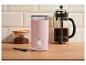 Różowy młynek do kawy, French press i kawa mielona na drewnianym blacie.