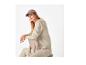 Kobieta w brązowej czapce i beżowej bluzie siedząca na krześle