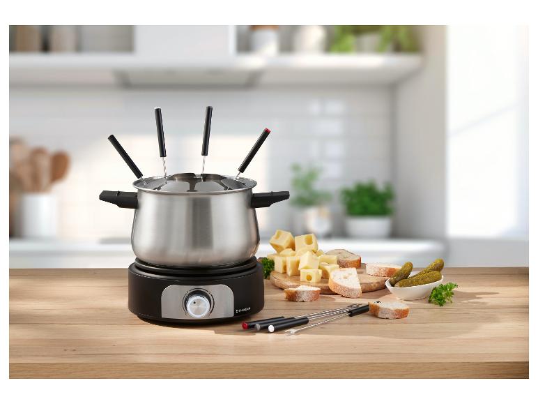 Zestaw do fondue z serem, chlebem i ogórkami na drewnianym stole w kuchni.