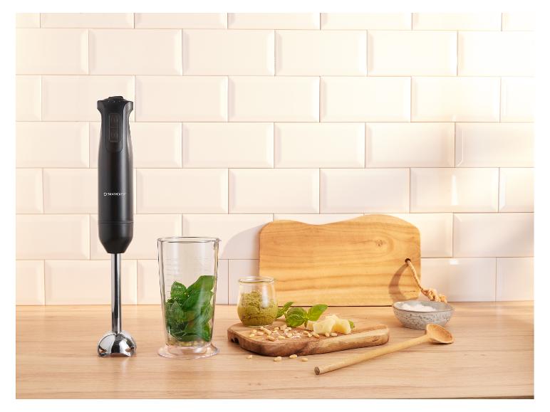 Blender ręczny ze składnikami na pesto na drewnianym blacie.