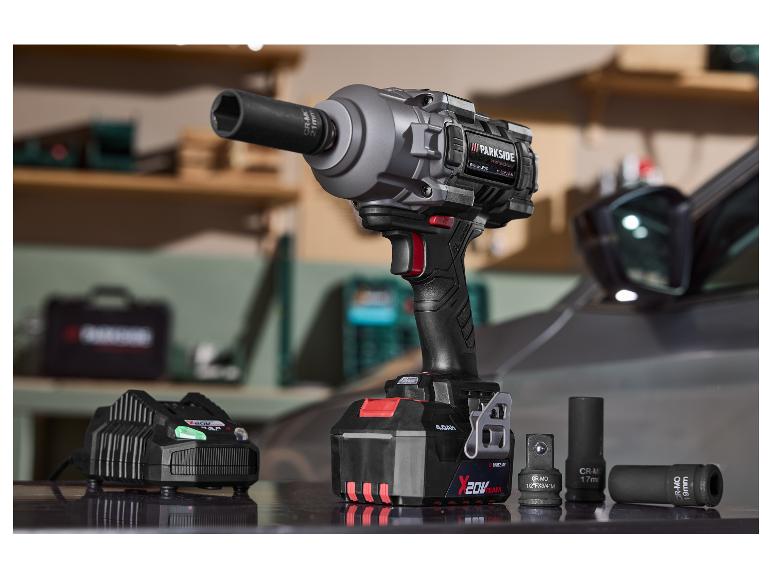 Klucz udarowy z akumulatorem, ładowarką i nasadkami, w tle samochód.