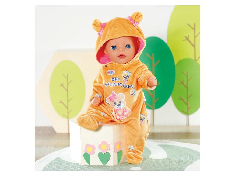 Lalka BABY born w pomarańczowym kostiumie pszczoły z napisem „OH, BEEAUTIFUL”, siedząca na pudełku.