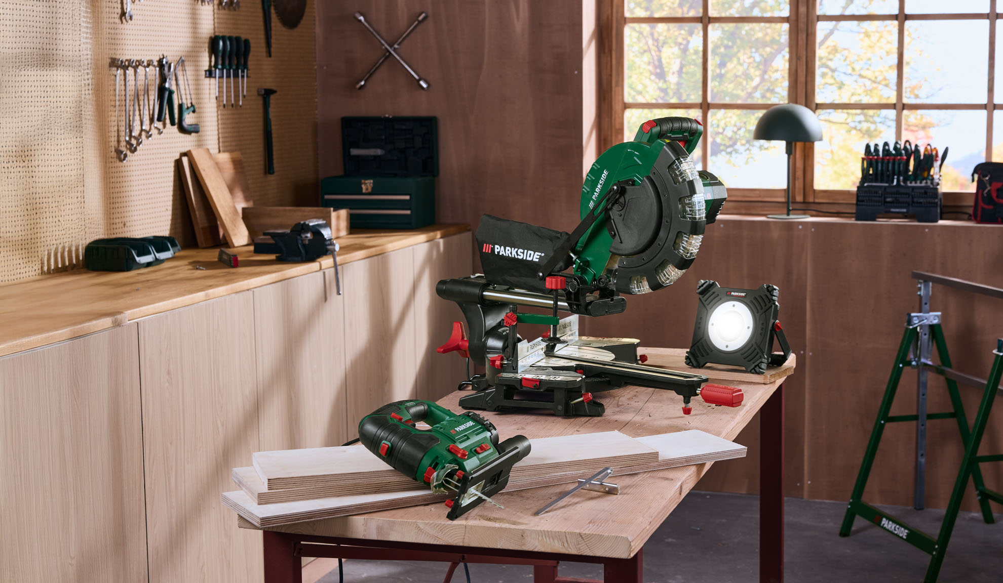 Ukośnica, wyrzynarka i lampa robocza na stole warsztatowym w pracowni.