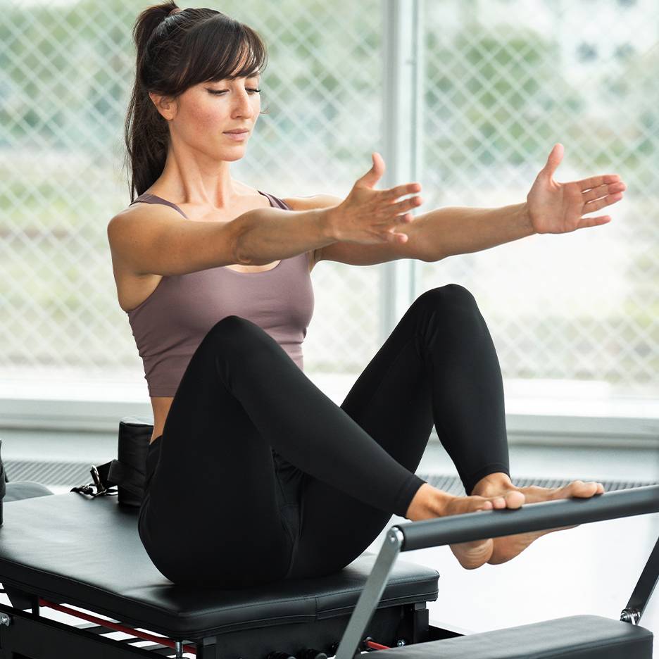 Kobieta ćwicząca Pilates na reformerze, w topie i czarnych legginsach.