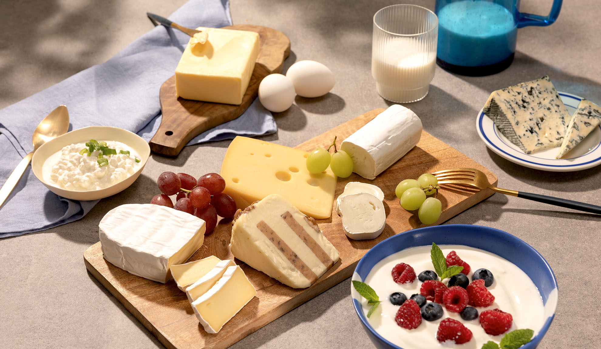 Różnorodne sery, winogrona i produkty mleczne, takie jak twaróg, mleko i jogurt z jagodami.