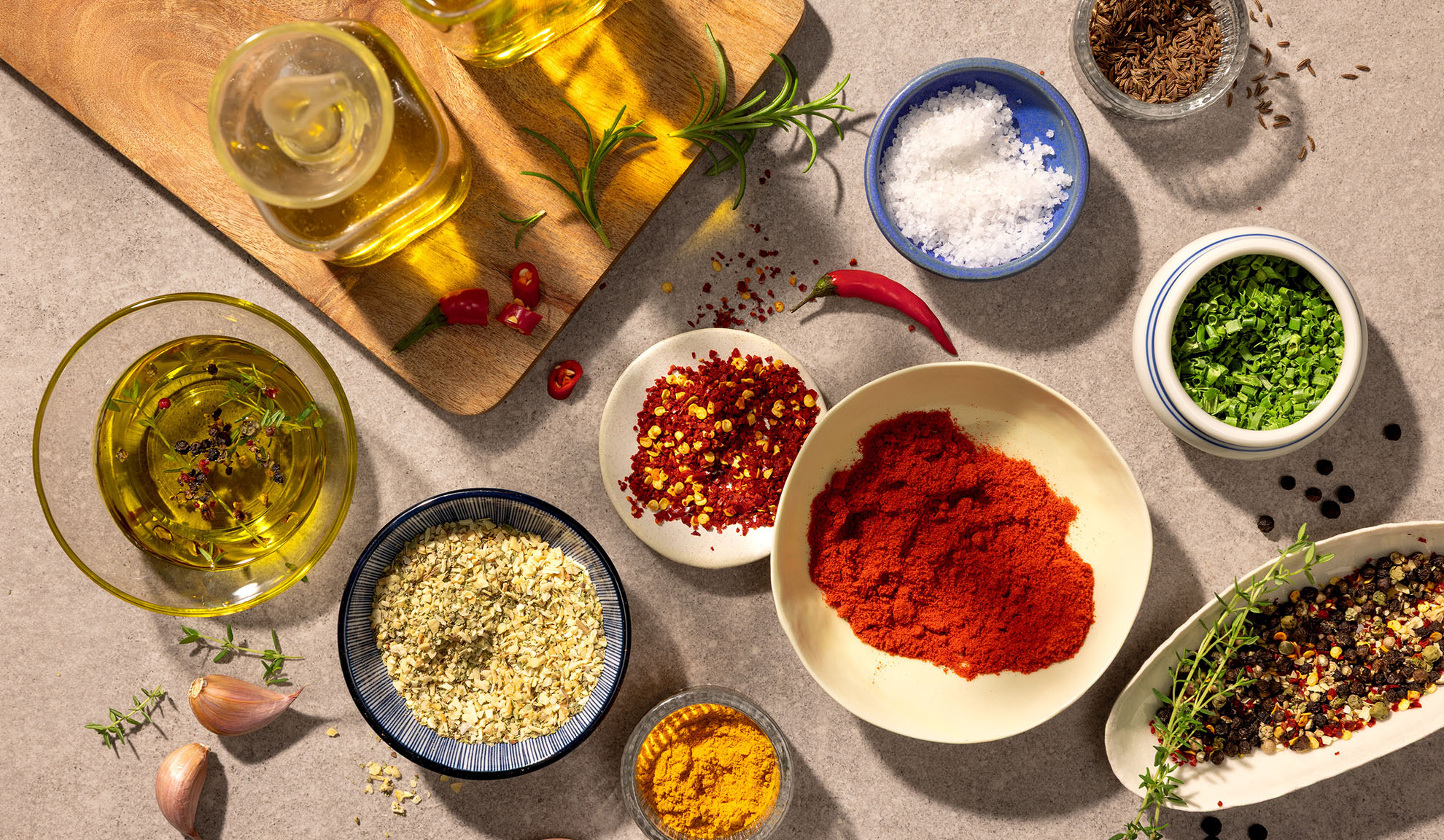 Widok z góry na różne przyprawy, zioła i oliwę z oliwek na szarej powierzchni.